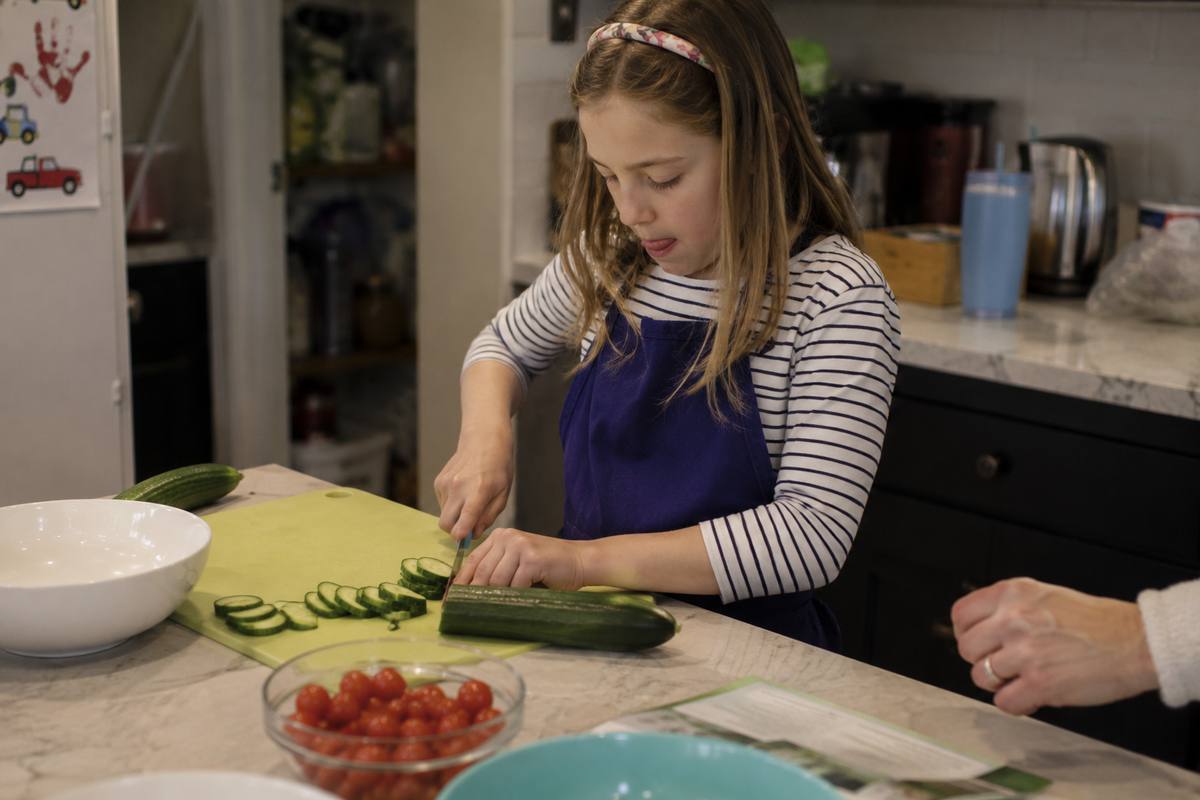 Child slicing cucumber with adult supervision in a kitchen